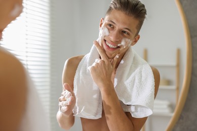 Photo of Man washing his face with cosmetic product near mirror in bathroom