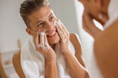 Photo of Man washing his face with cosmetic product near mirror in bathroom