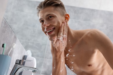 Photo of Happy man washing his face in bathroom, low angle view