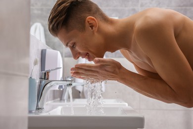 Photo of Happy man washing his face over sink in bathroom