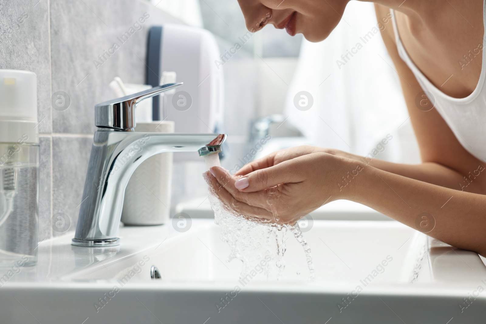 Photo of Woman washing her face over sink in bathroom, closeup