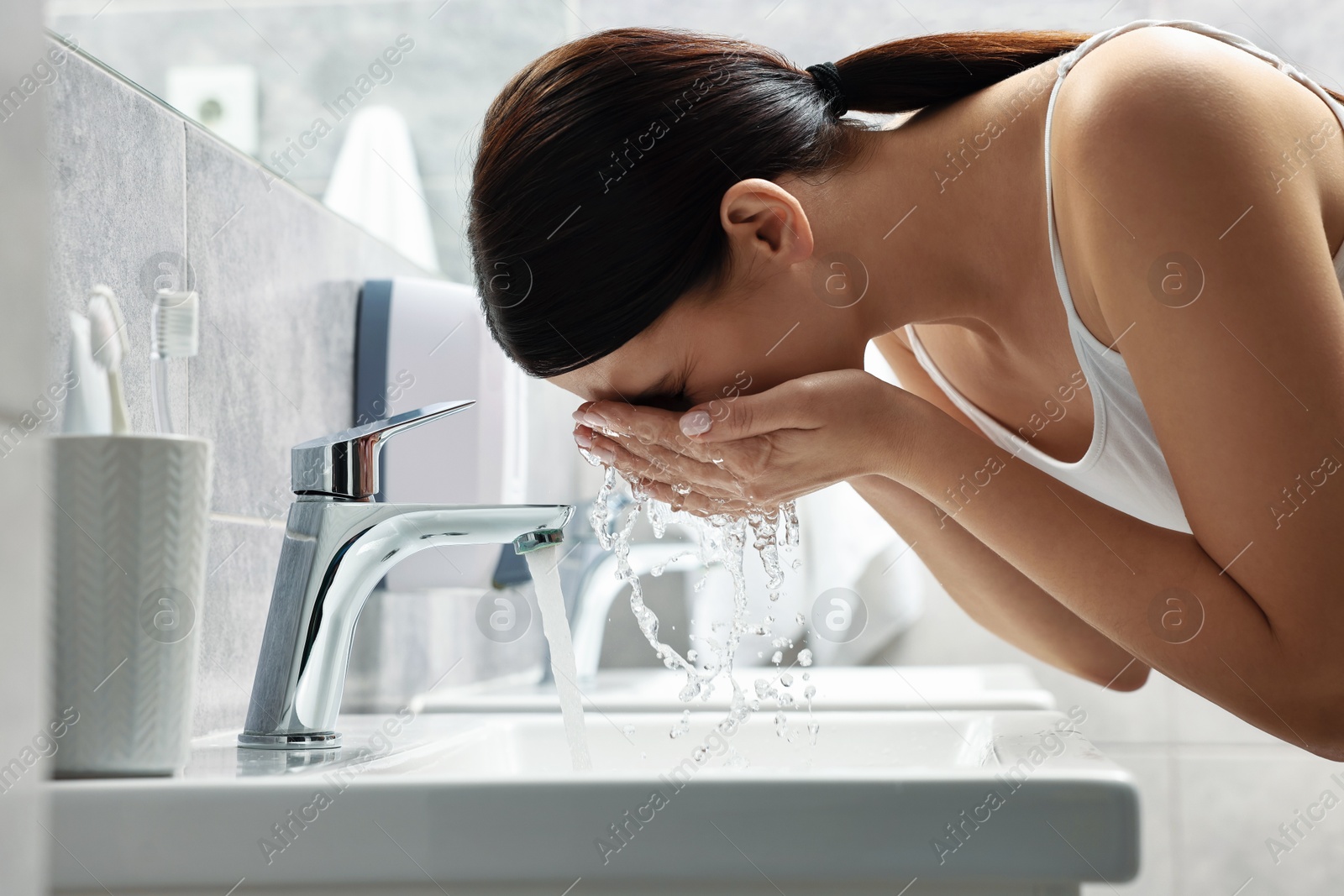 Photo of Woman washing her face over sink in bathroom