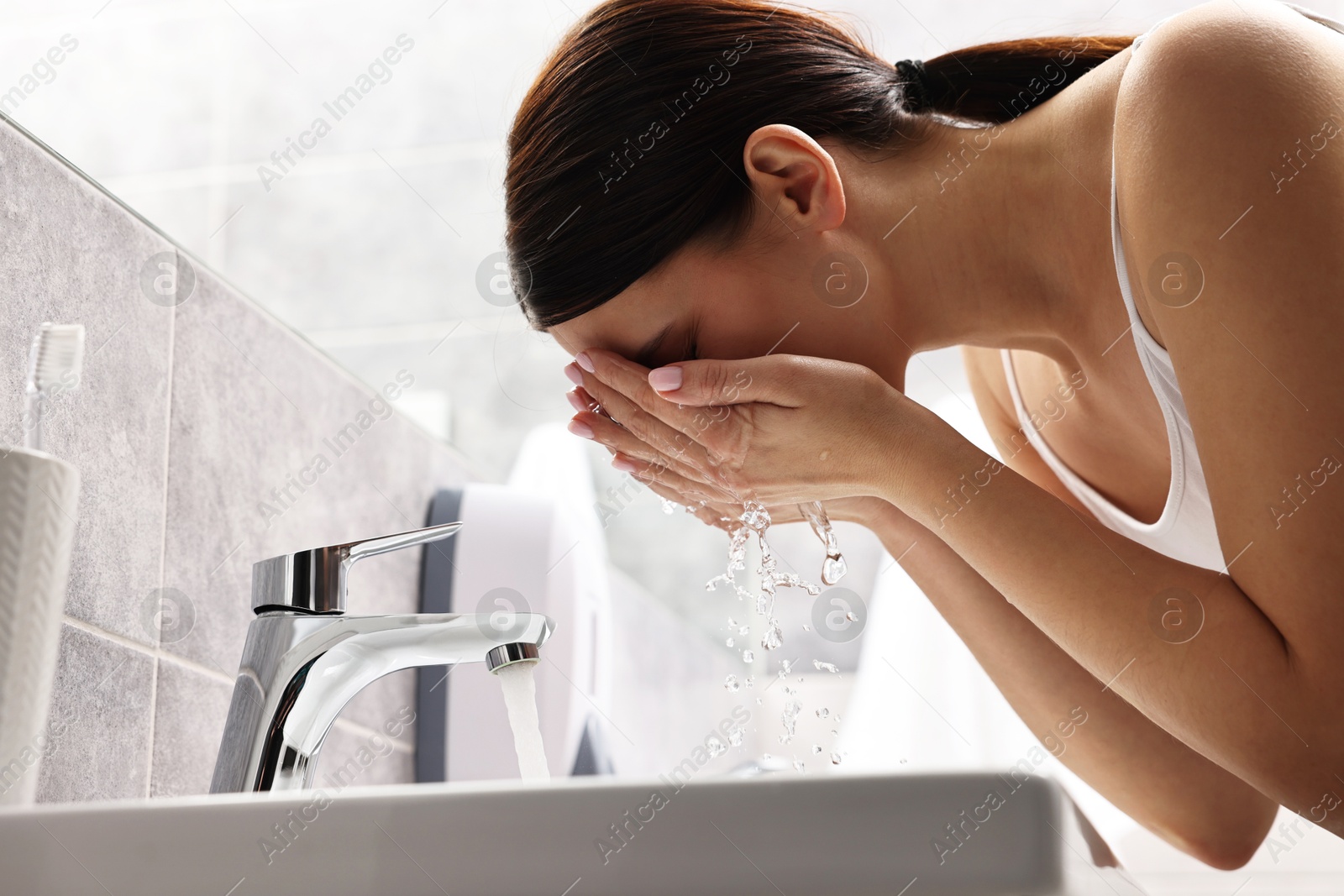 Photo of Woman washing her face over sink in bathroom, low angle view