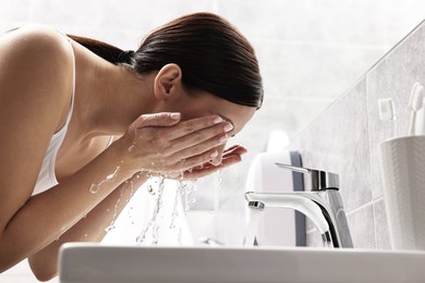 Photo of Woman washing her face over sink in bathroom