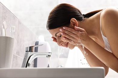 Photo of Woman washing her face over sink in bathroom