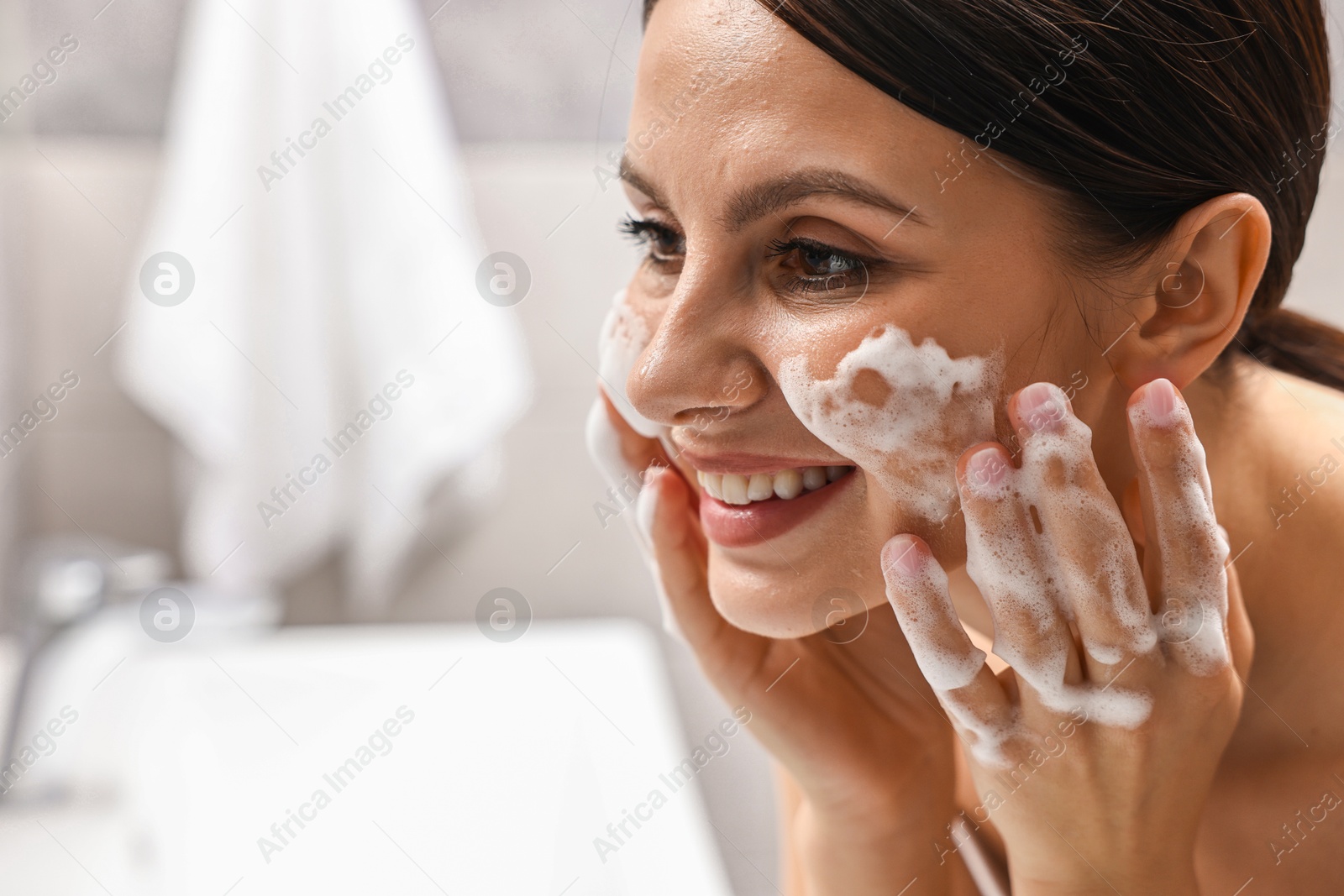 Photo of Woman washing her face with cleansing foam in bathroom, space for text