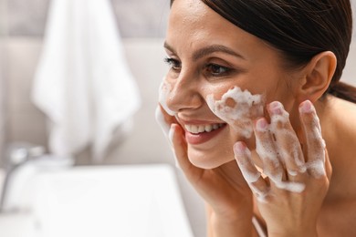 Photo of Woman washing her face with cleansing foam in bathroom, space for text