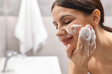 Photo of Woman washing her face with cleansing foam in bathroom, space for text