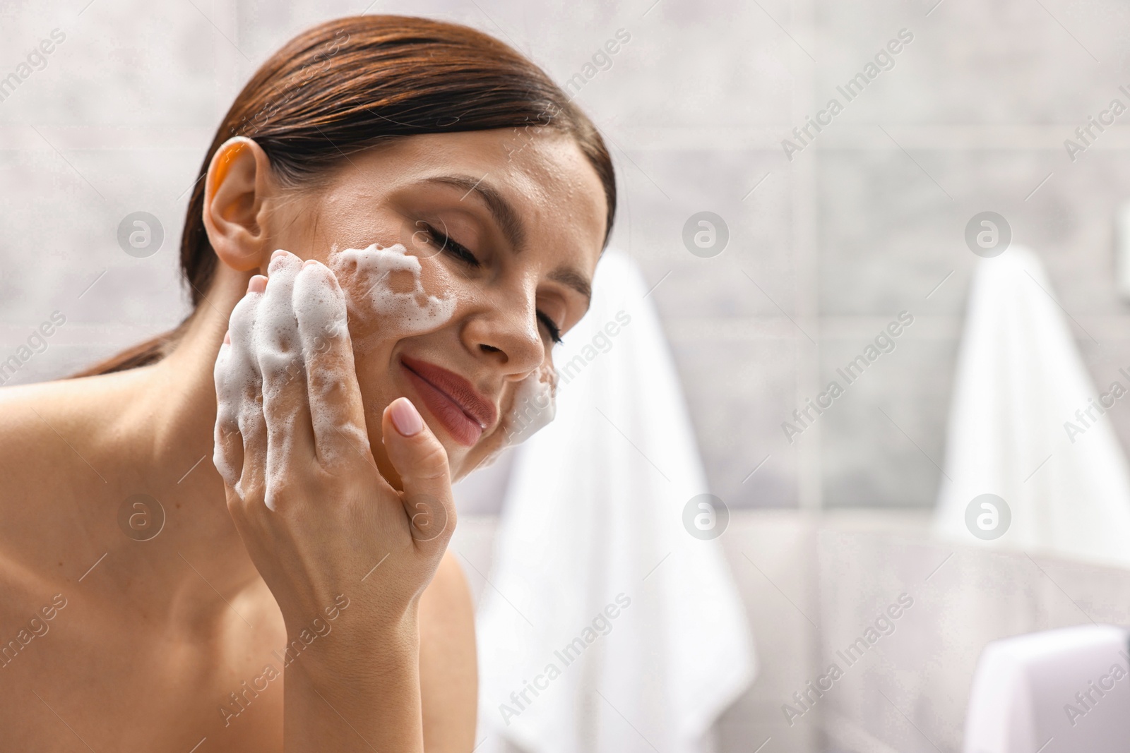 Photo of Woman washing her face with cleansing foam in bathroom, space for text