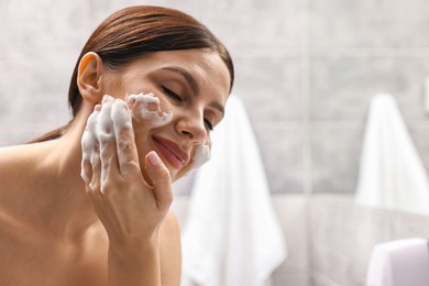 Photo of Woman washing her face with cleansing foam in bathroom, space for text