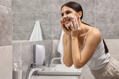 Photo of Woman washing her face with cleansing foam in bathroom