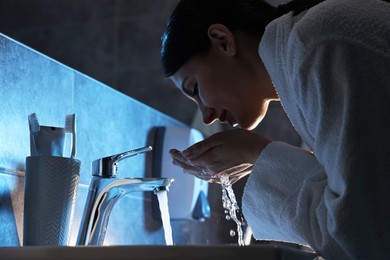 Photo of Woman washing her face over sink in bathroom