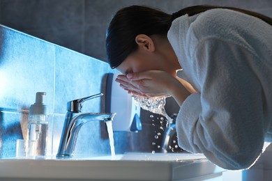 Photo of Woman washing her face over sink in bathroom