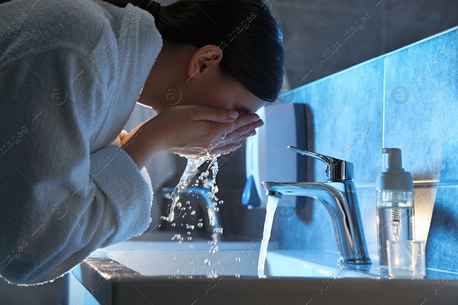 Photo of Woman washing her face over sink in bathroom