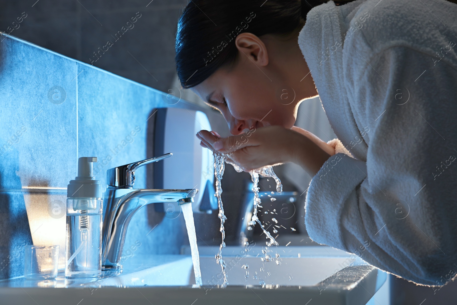 Photo of Woman washing her face over sink in bathroom