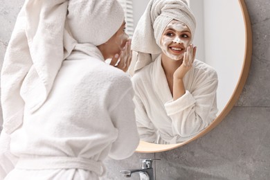 Photo of Woman washing her face with cleansing foam near mirror in bathroom