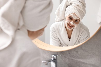 Photo of Woman washing her face with cleansing foam near mirror in bathroom