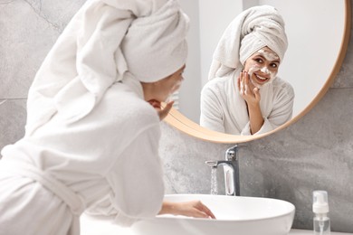 Photo of Woman washing her face with cleansing foam near mirror in bathroom