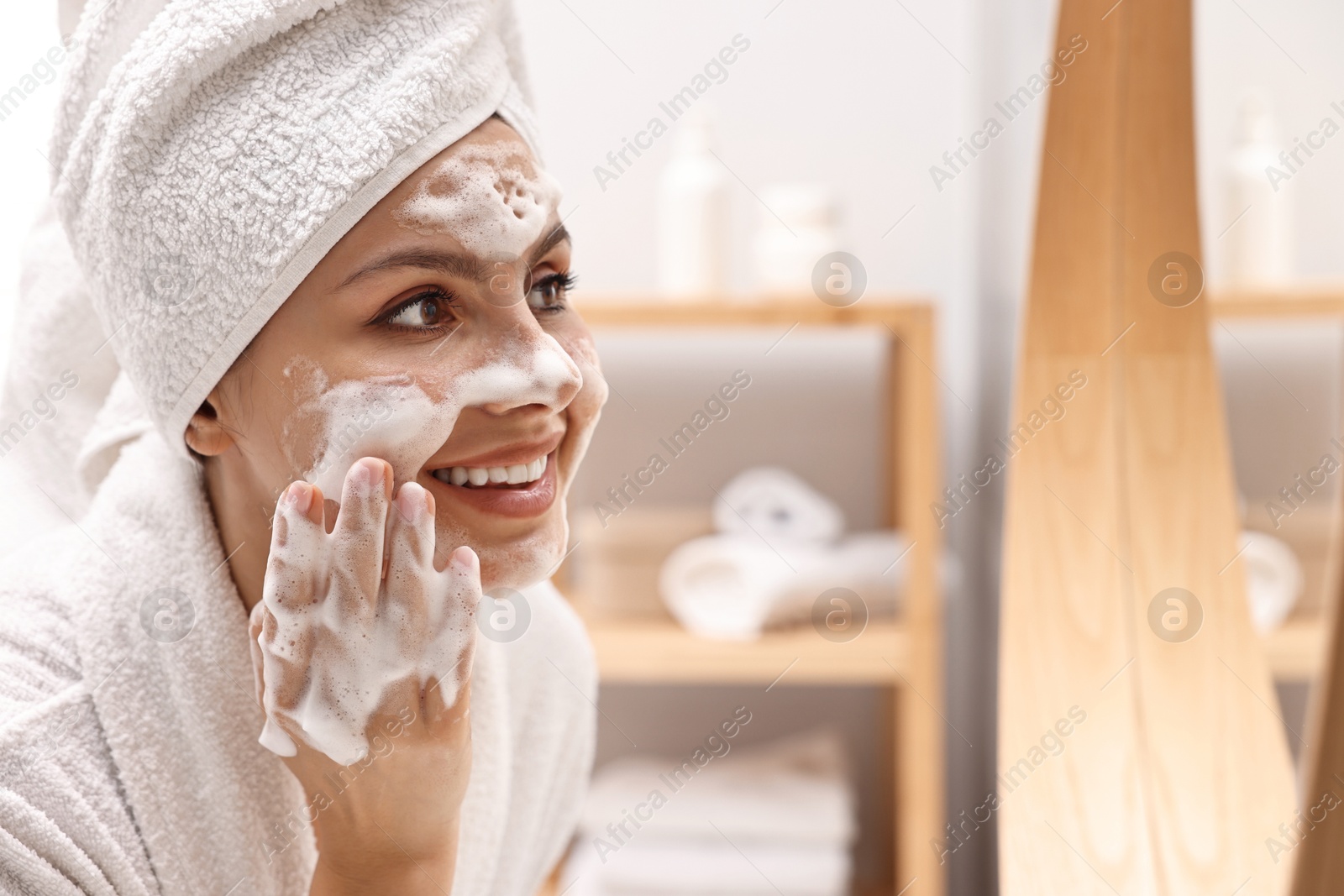 Photo of Woman washing her face with cleansing foam in bathroom, space for text