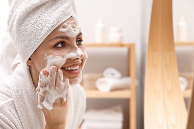 Woman washing her face with cleansing foam in bathroom, space for text