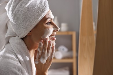 Photo of Woman washing her face with cleansing foam in bathroom