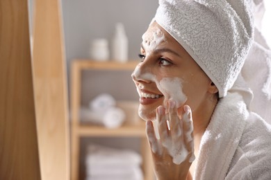 Photo of Woman washing her face with cleansing foam in bathroom