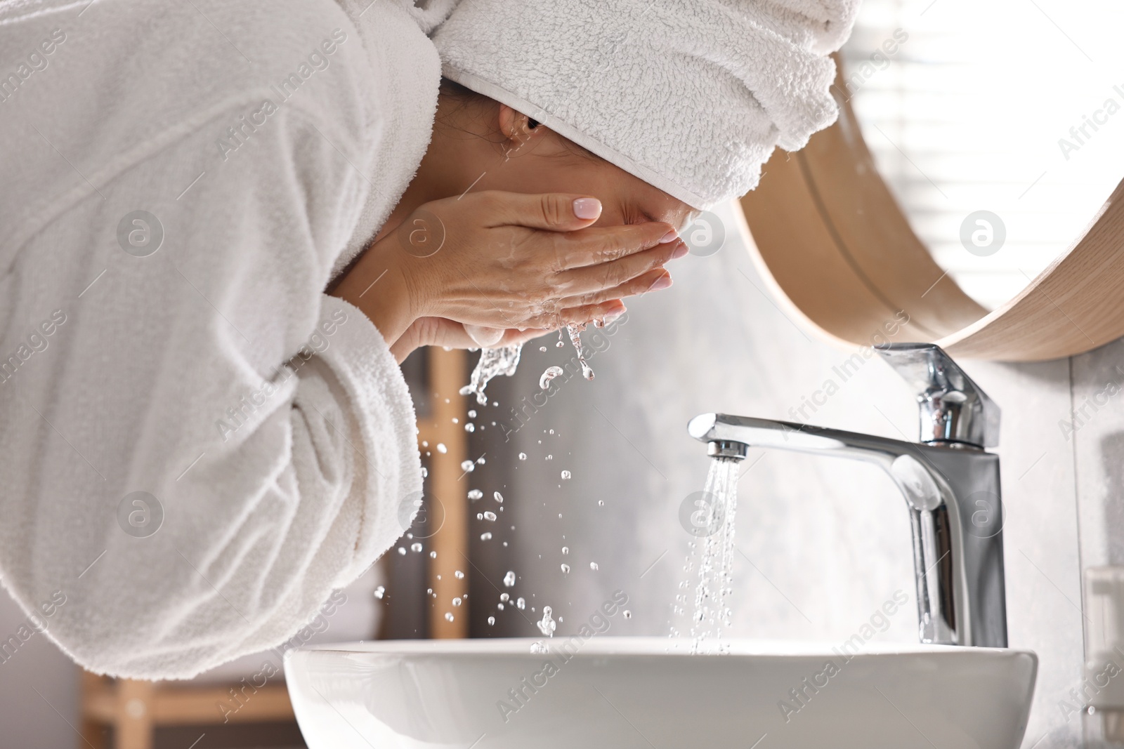 Photo of Woman washing her face over sink in bathroom