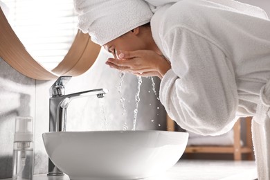 Photo of Woman washing her face over sink in bathroom