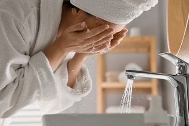 Photo of Woman washing her face over sink in bathroom