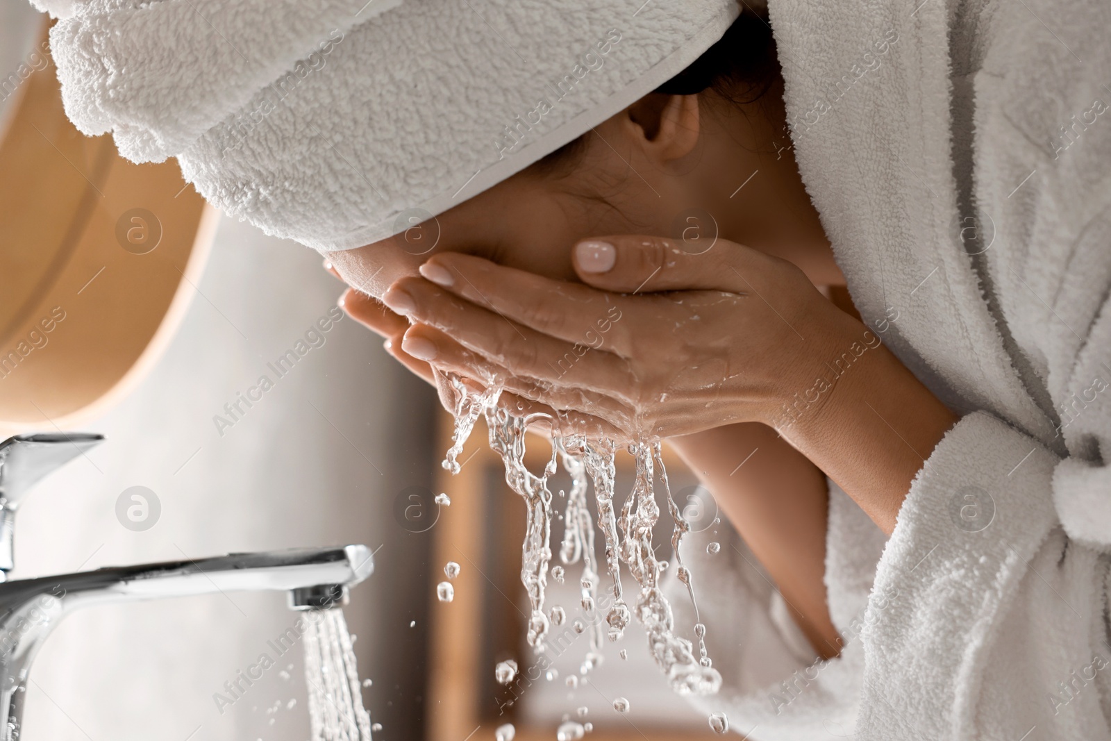 Photo of Woman in bathrobe washing her face in bathroom