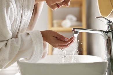 Photo of Woman washing her face over sink in bathroom, closeup