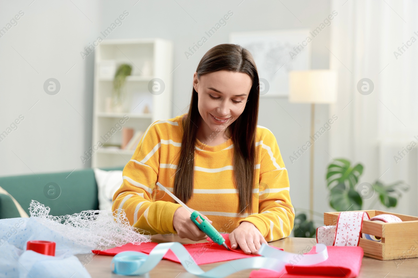 Photo of Woman with hot glue gun making craft at table indoors