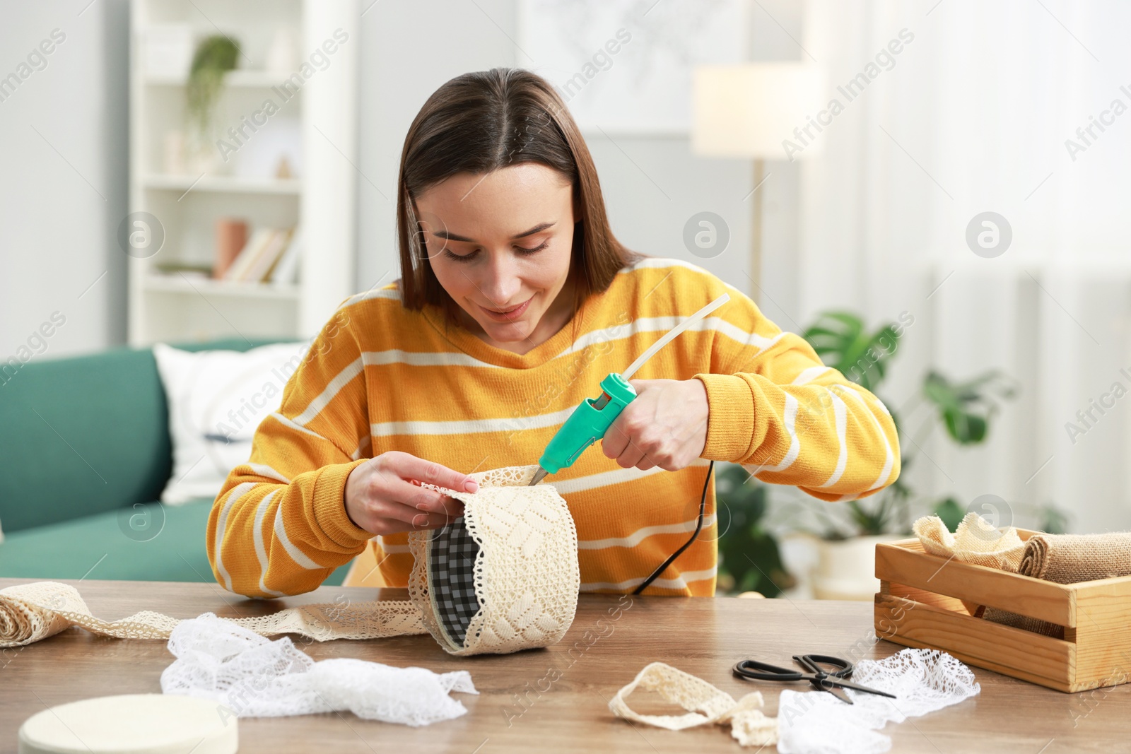 Photo of Woman with hot glue gun making craft at table indoors