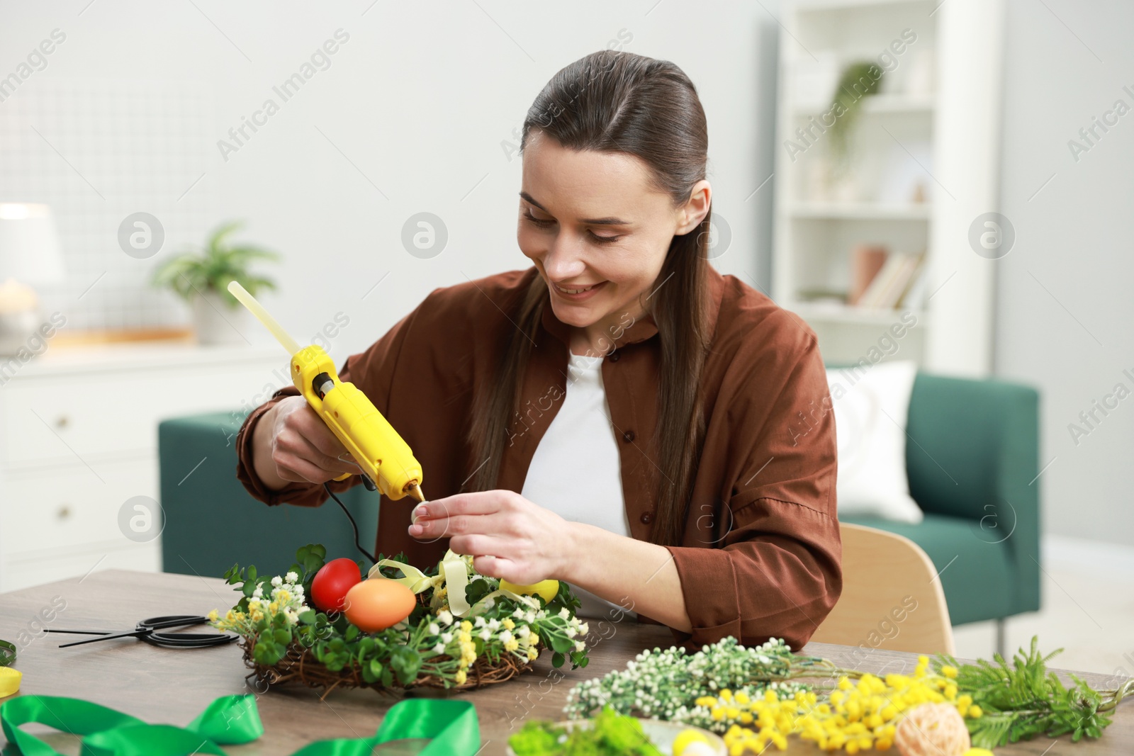 Photo of Woman with hot glue gun making craft at table indoors