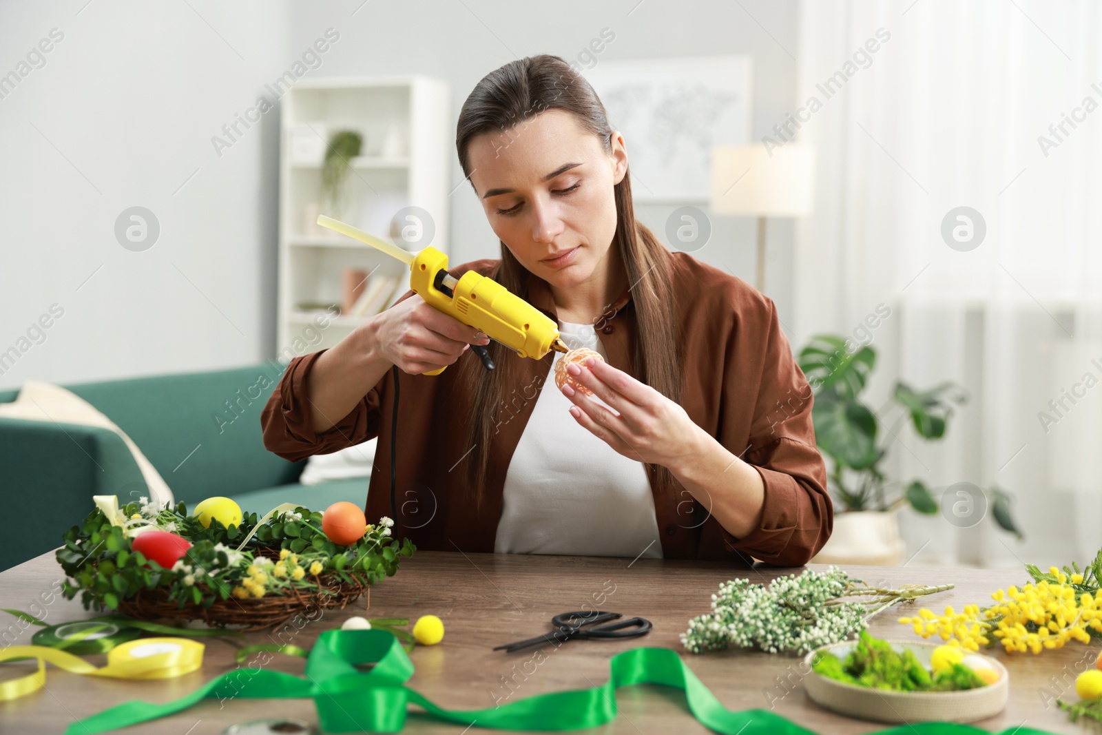 Photo of Woman with hot glue gun making craft at table indoors