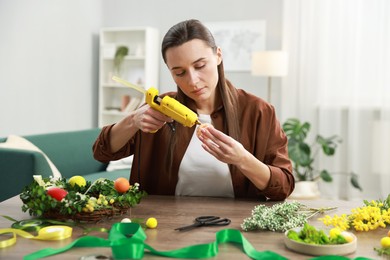 Woman with hot glue gun making craft at table indoors