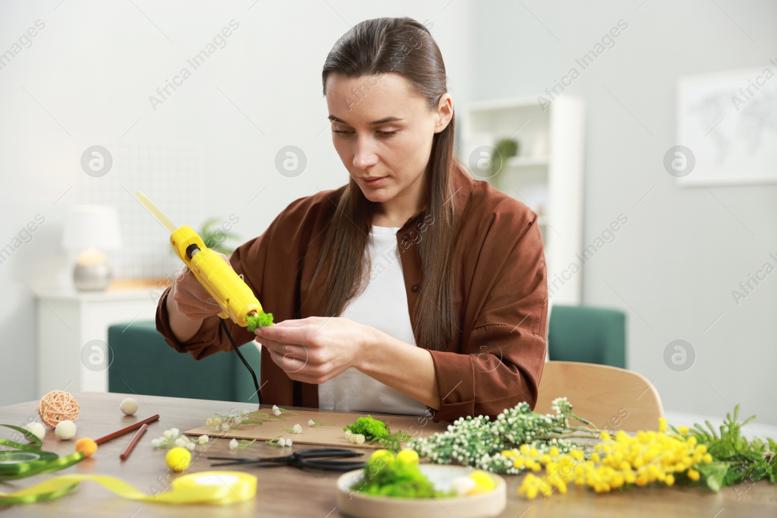 Photo of Woman with hot glue gun making craft at table indoors