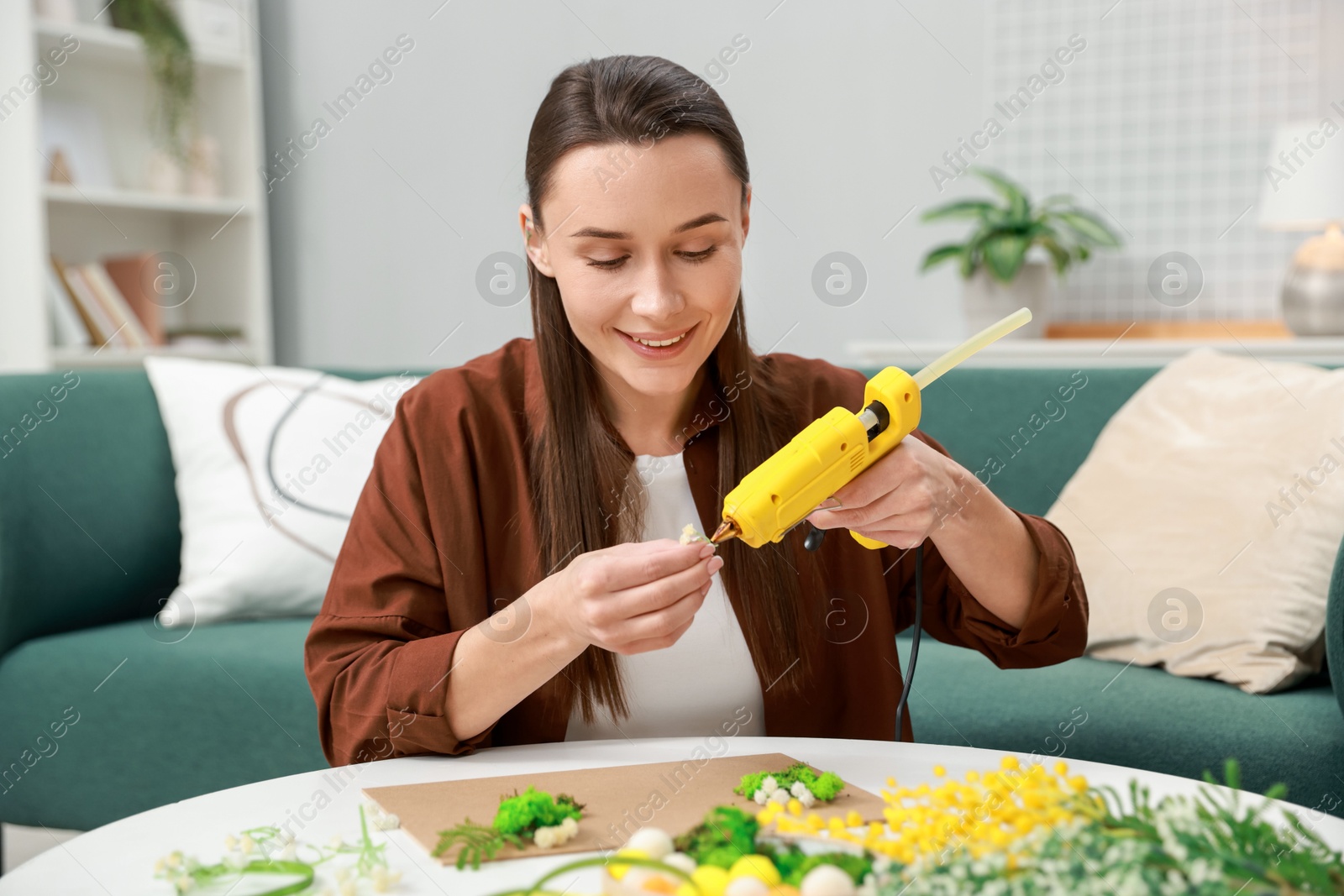 Photo of Woman with hot glue gun making craft at table indoors