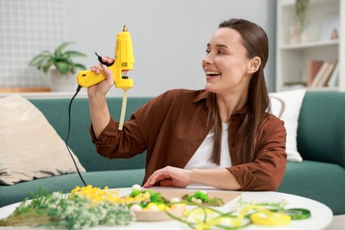 Photo of Woman with hot glue gun making craft at table indoors