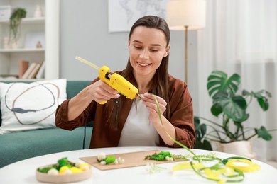 Photo of Woman with hot glue gun making craft at table indoors