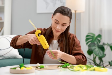 Photo of Woman with hot glue gun making craft at table indoors