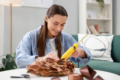 Photo of Woman with hot glue gun making craft at table indoors