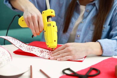 Photo of Woman with hot glue gun making craft at table indoors, closeup