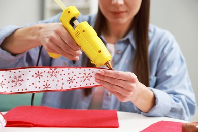 Photo of Woman with hot glue gun making craft at table indoors, closeup