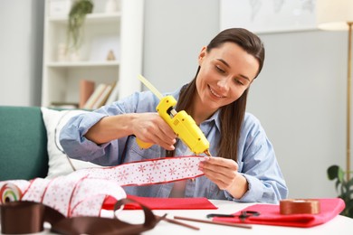 Photo of Woman with hot glue gun making craft at table indoors