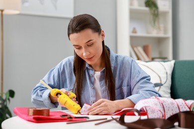 Photo of Woman with hot glue gun making craft at table indoors