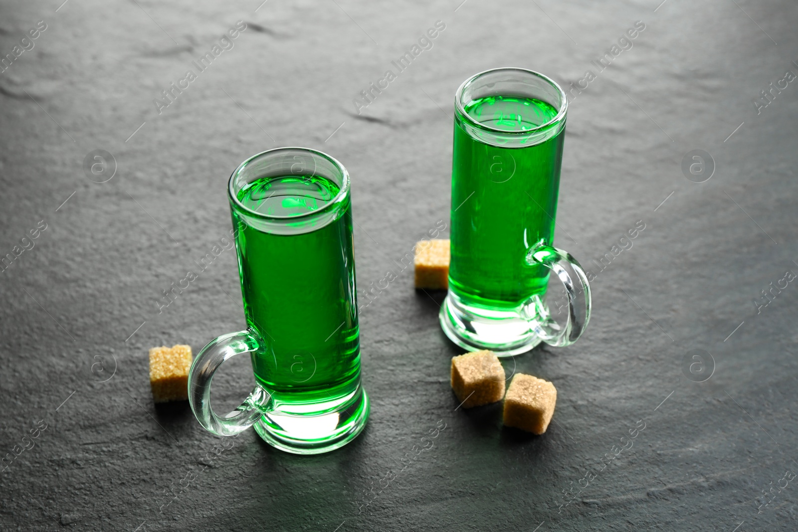 Photo of Delicious absinthe in shot glasses and brown sugar cubes on grey textured table, closeup