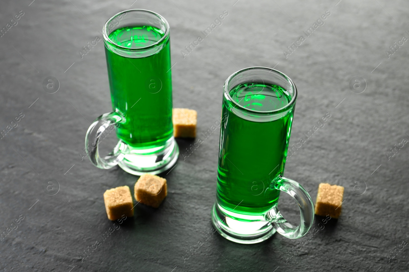 Photo of Delicious absinthe in shot glasses and brown sugar cubes on grey textured table, closeup