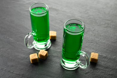 Photo of Delicious absinthe in shot glasses and brown sugar cubes on grey textured table, closeup