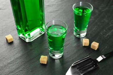 Photo of Delicious absinthe, spoon and brown sugar cubes on grey textured table, closeup